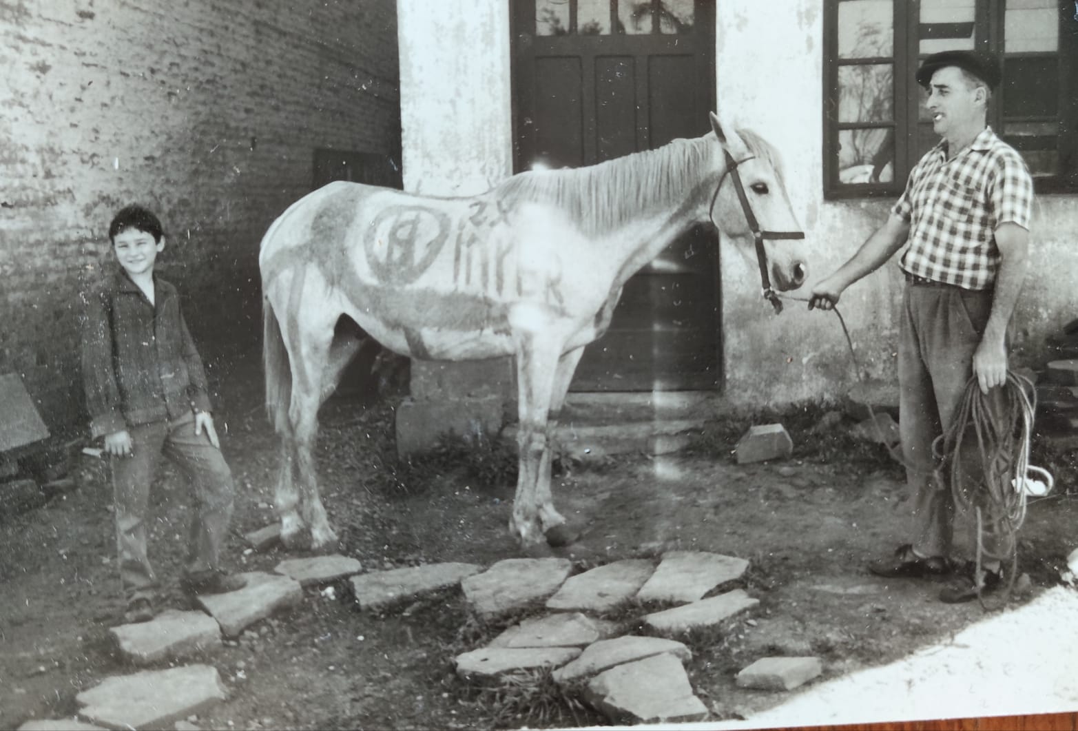 Foto antiga em preto e branco de um menino e um homem ao lado de um cavalo